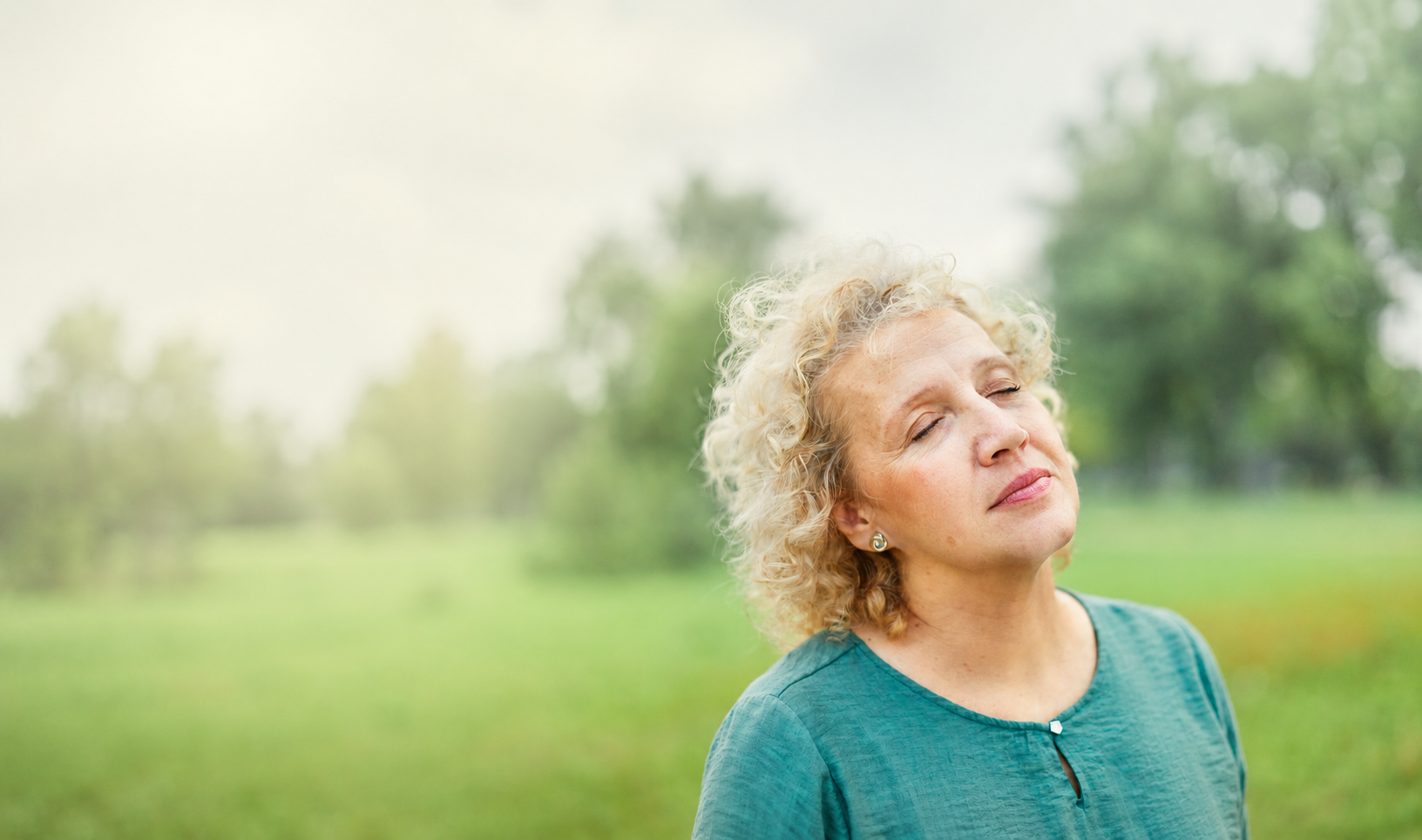 woman with eyes closed standing outside landscape